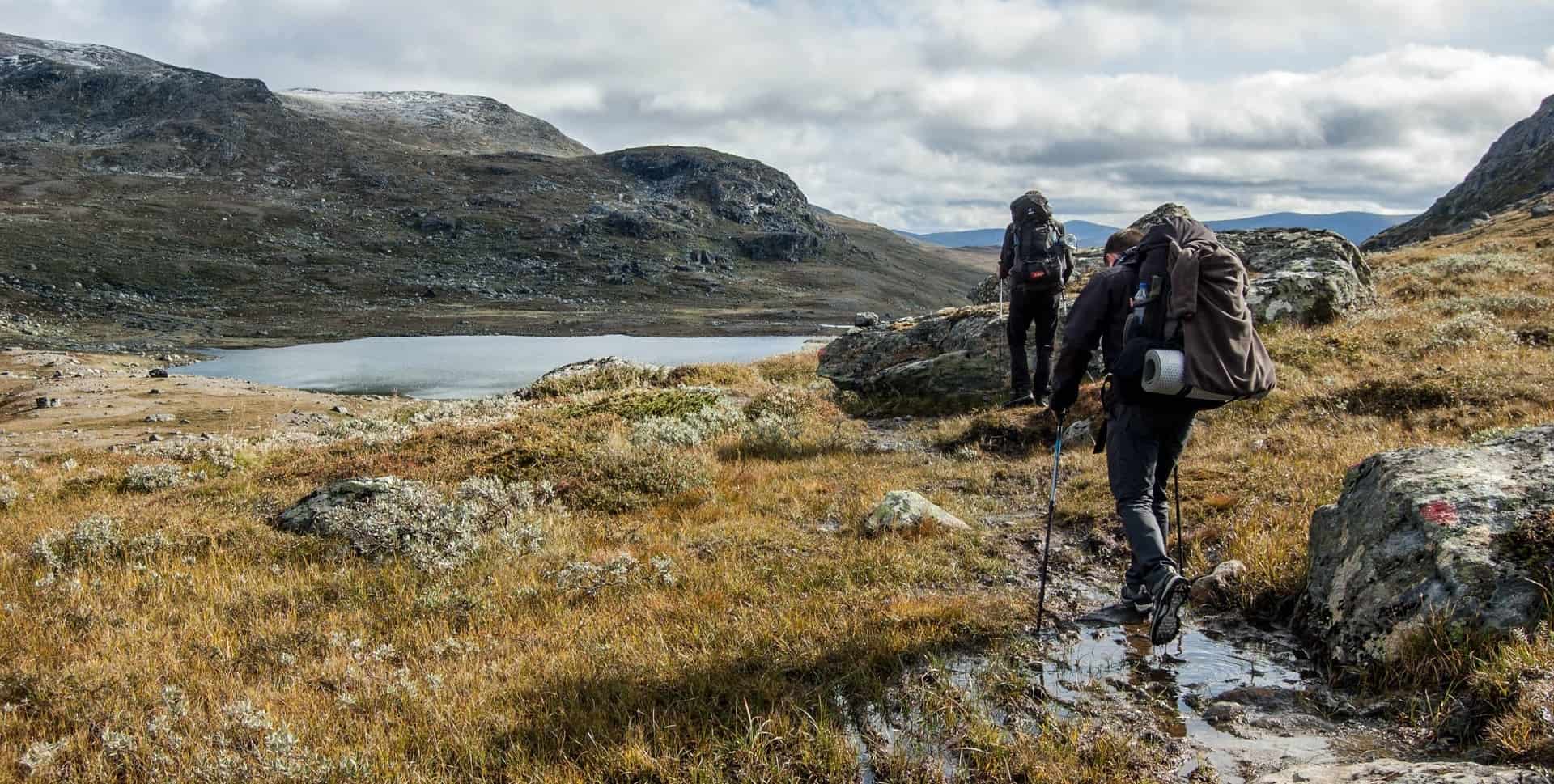 Two men with laden backpacks crossing a mountain stream using trekking poles. when backpacking outdoors