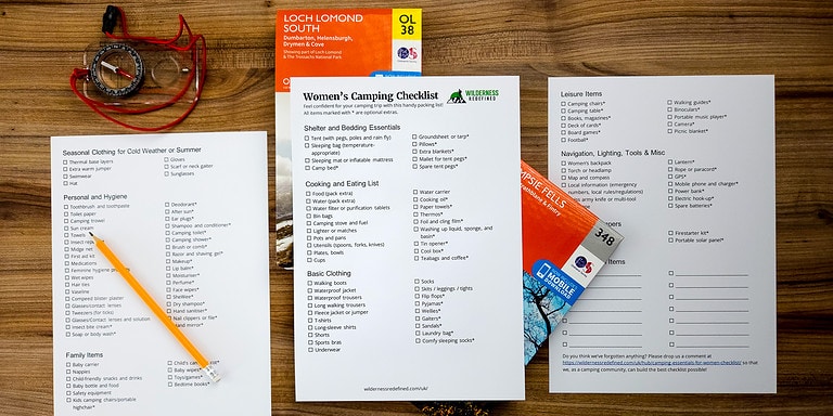 A printed women's camping essentials checklist for female campers lying beside a map and compass