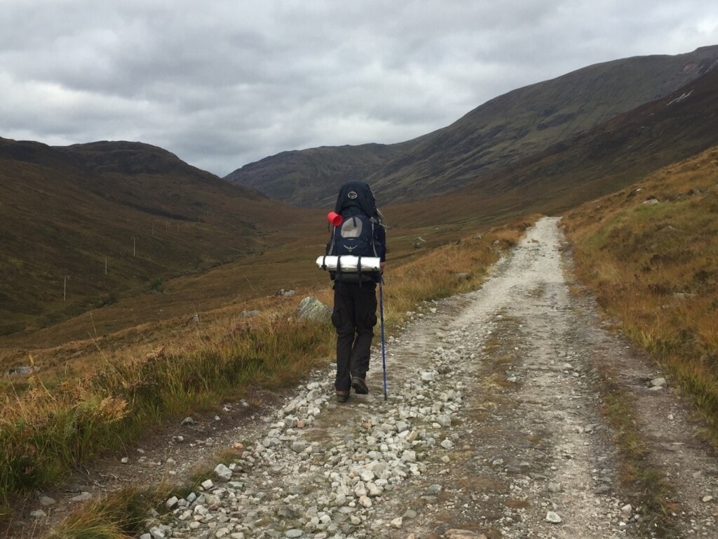 A hiker walks up a mountainous hillside in scotland carrying a backpack