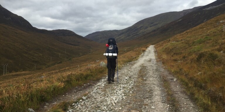 A hiker walks up a mountainous hillside in Scotland carrying a backpack
