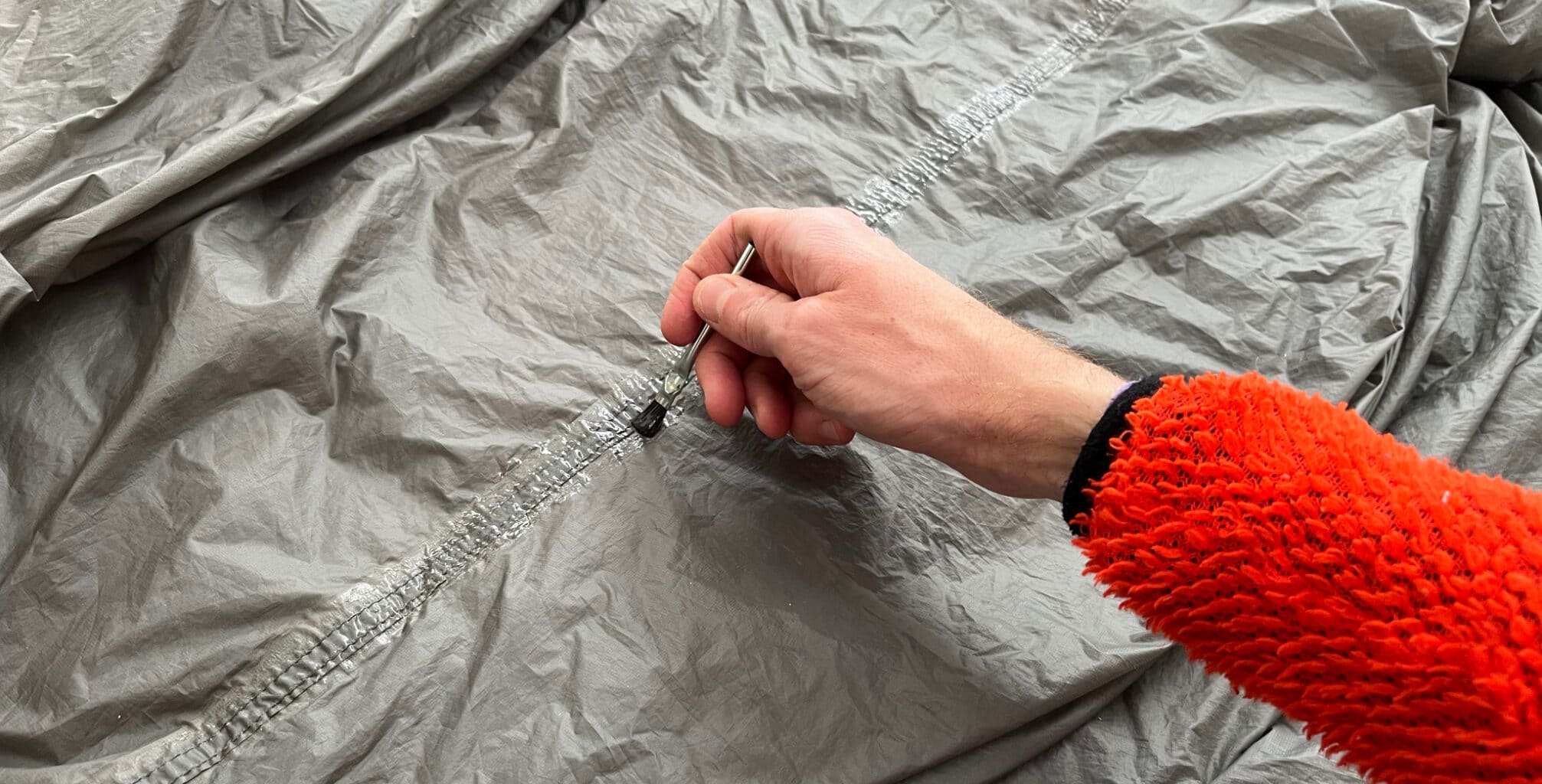 a person uses a brush to evenly distribute seam sealant along the seam of a tent