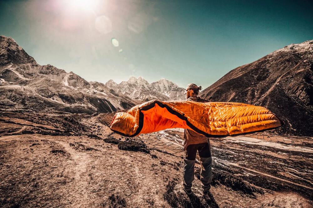 A man shaking out a sleeping bag to get rid of the moisture in it