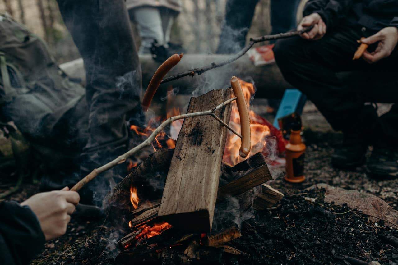 Camping enthusiasts cooking sausages and making coffee over a small campfire