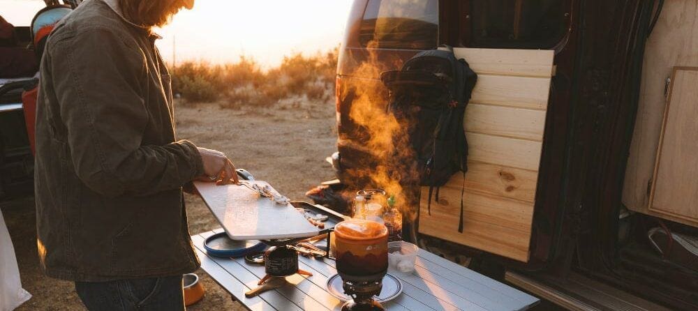 Man putting chopped mushrooms into a Jetboil stove at a campsite 