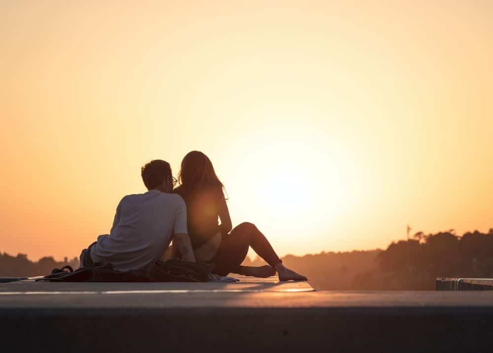 A couple sitting on a jetty at Sunset creating romance and having fun.