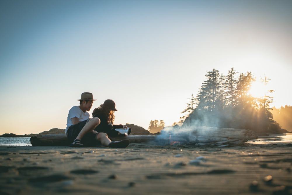 A couple reading a book on a beach with a campfire