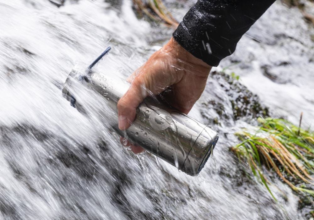 Person refilling a water bottle in a stream