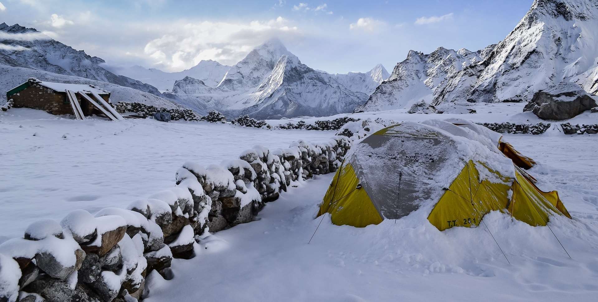 A yellow camping tent covered in a light dusting of snow on a cold mountain