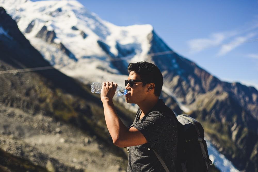 Man drinking from a bottle while hiking in the mountains