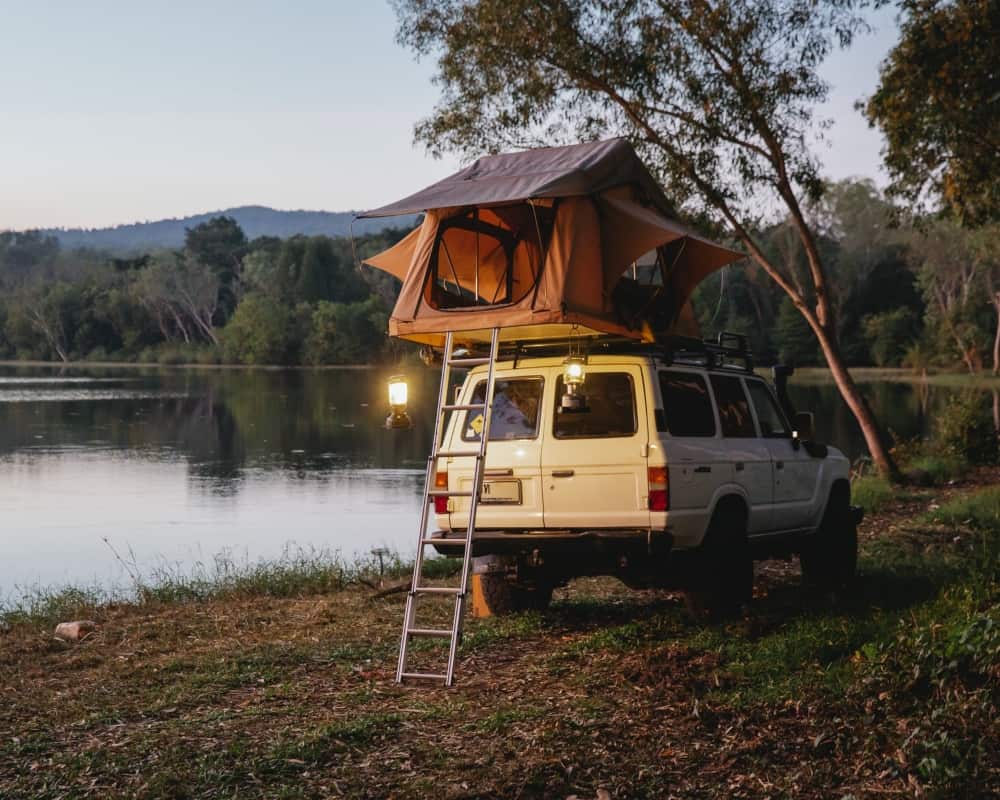 A rooftop tent set up on an SUV while camping beside a lake