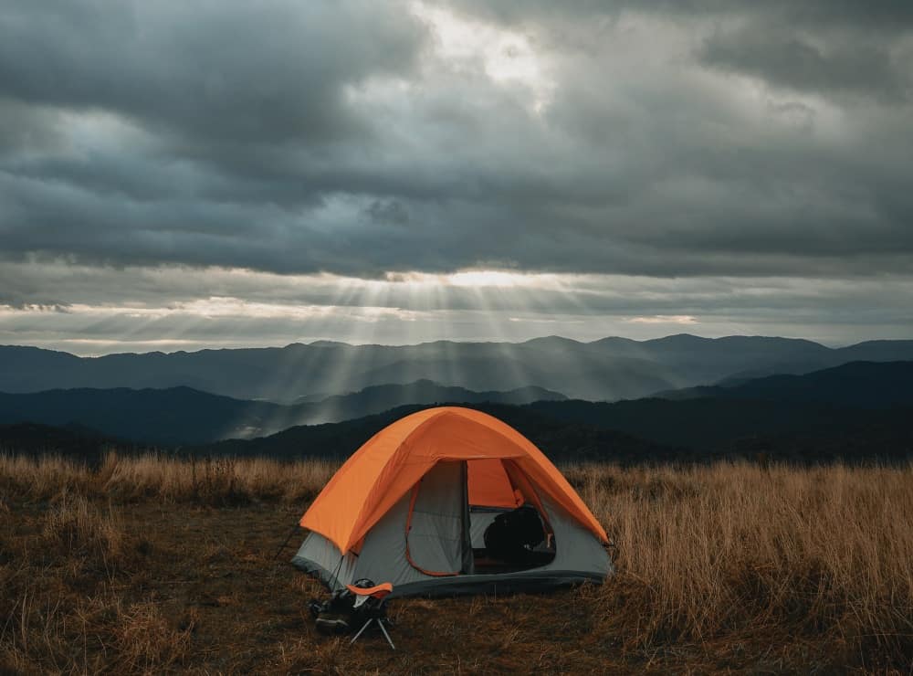 Orange tent in a field with the sun shining down