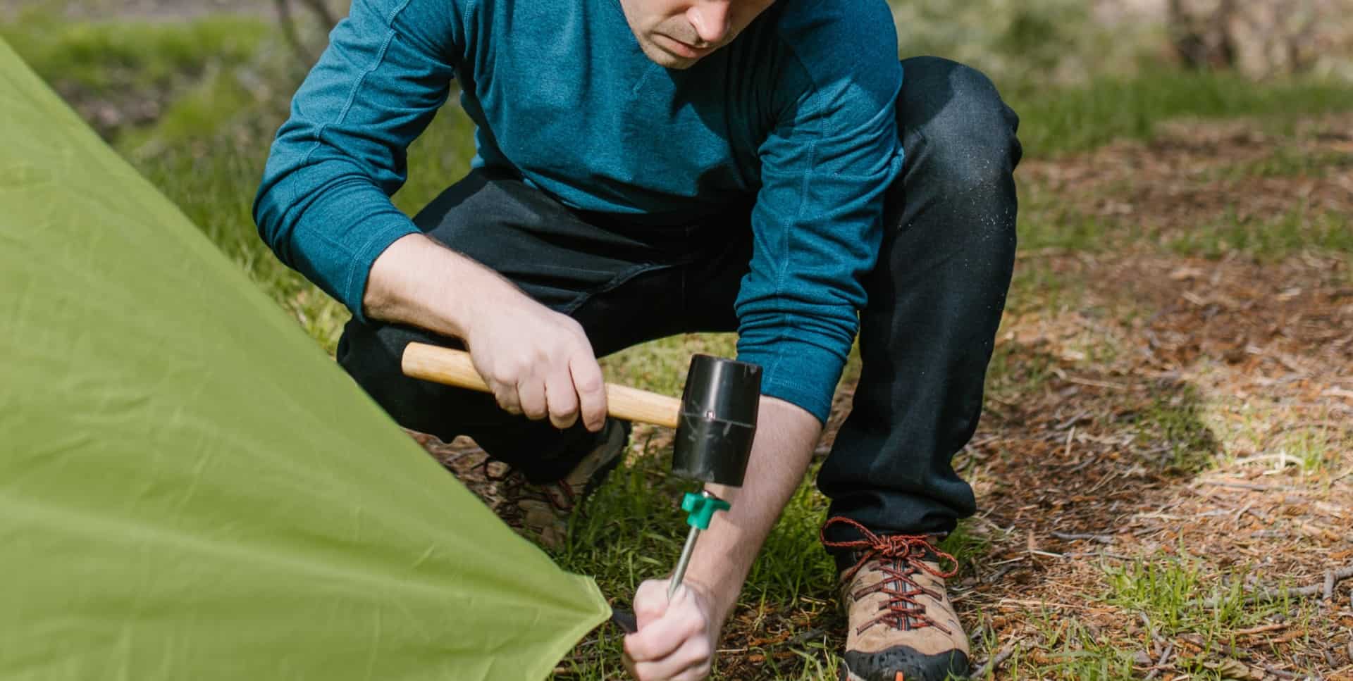 Man putting tent peg into the ground of a green tent