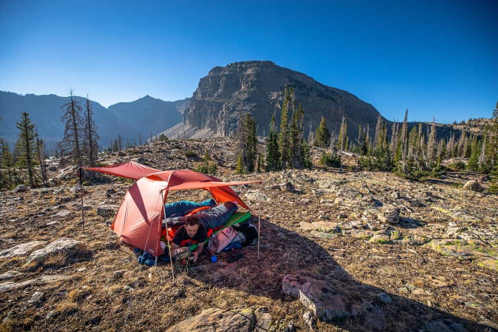 A man inside a free standing single-wall tent pitched on a mountain plateau