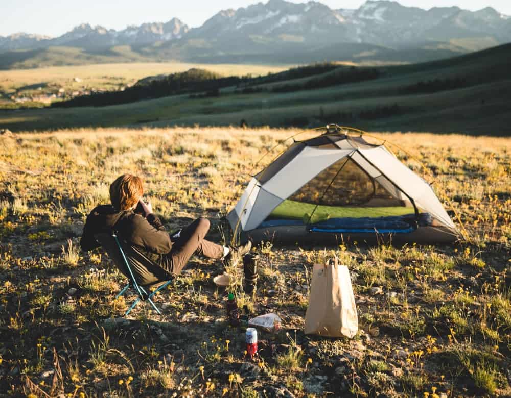 Man on a chair next to a mesh tent on a mountain meadow