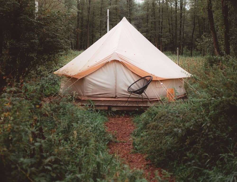 A round canvas tent sitting on a wooden platform with a canvas rainfly on top of the tent.