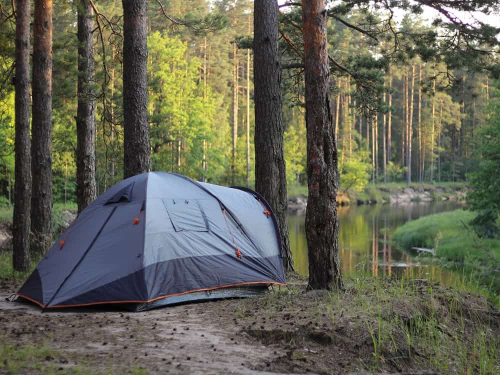 Gray double walled tent with a fly set up by a river
