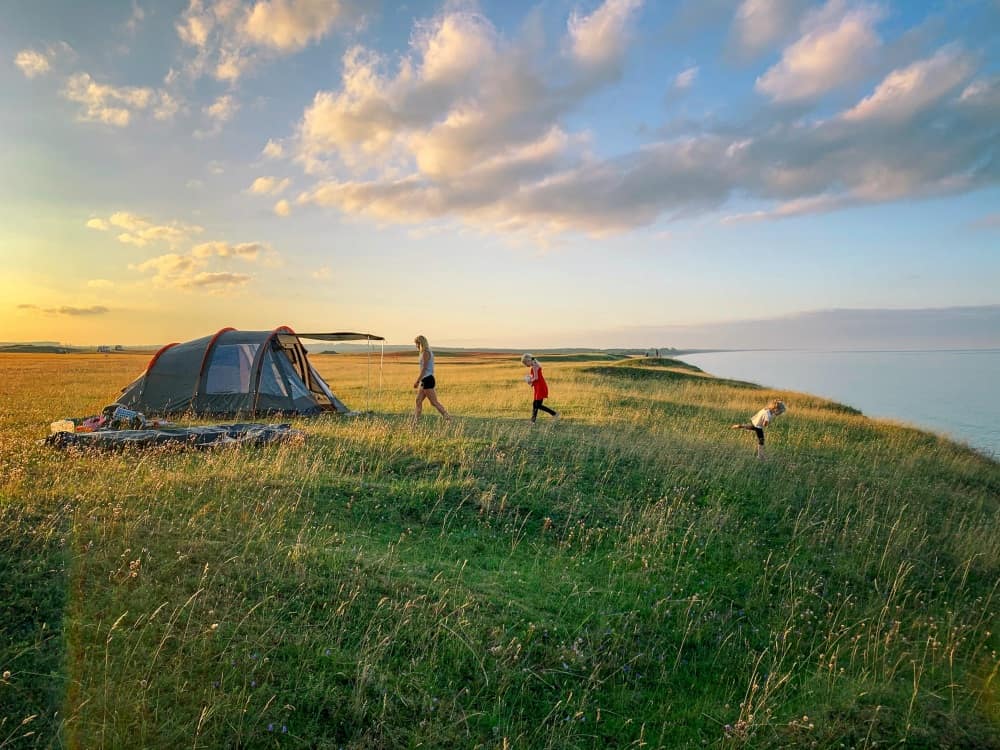 A single walled tent set up in a meadow with a family.