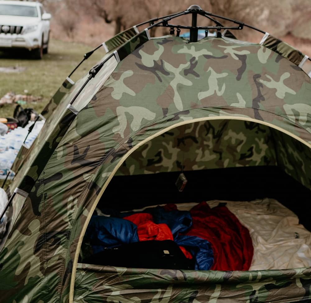 Camo instant tent pitched in a paddock by a car