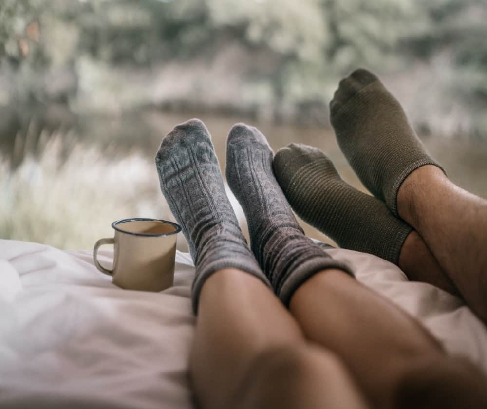 A couple’s feet with socks and a hot drink at a tent entrance.