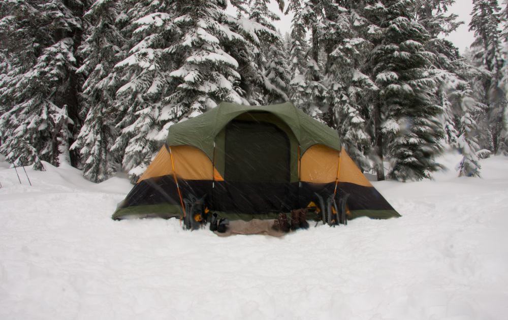 Four-season tent set up in the snow with gear outside.