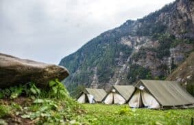 Three canvas A-frame tents set up in a mountain campsite