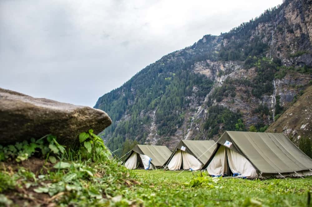 Three canvas A-frame tents set up in a mountain campsite