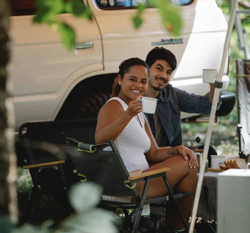 A couple enjoying a drink at their campsite and acknowledging the photographer.