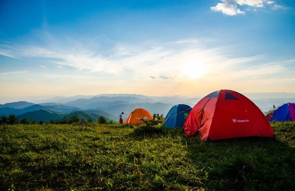 Four tents pitched on a hilltop overlooking a hilly view.