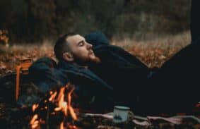 Man resting by a campfire under fall trees.