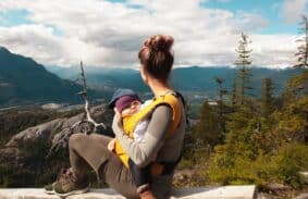 A mother carrying her baby on a camping trip while looking at a mountain