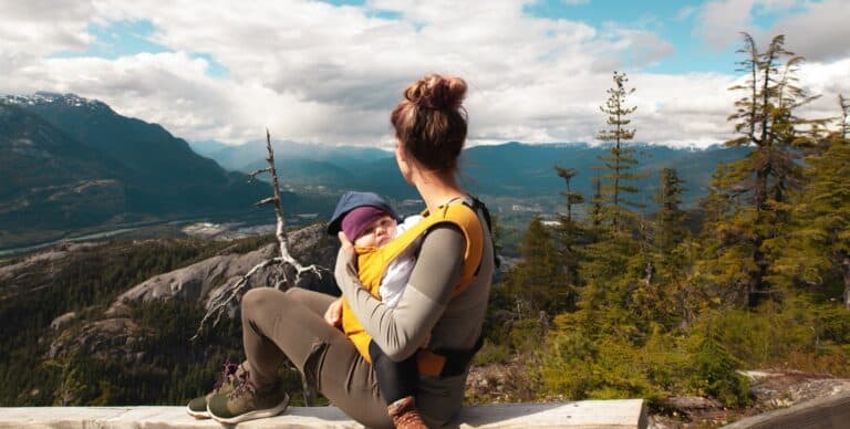 A mother carrying her baby on a camping trip while looking at a mountain