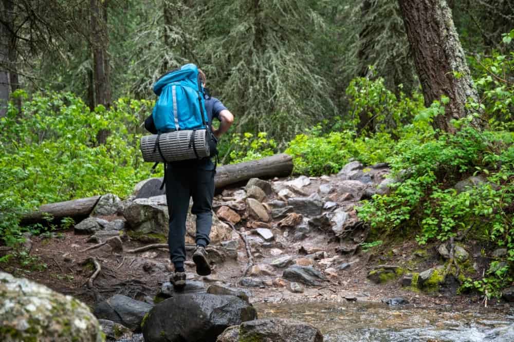 Backpacker with a full backpack trekking across a stream while hiking in the forest.