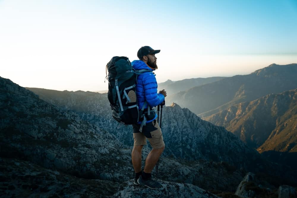 Backpacker with laden backpack contemplating the view from a rocky crag on a mountain.