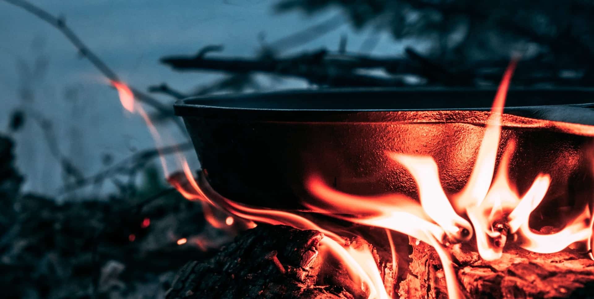 Cast iron pan cooking on the campfire by a lake at dusk.