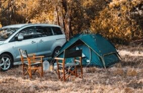 Tent and campsite set up next to a car in a meadow.
