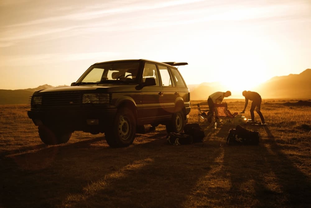 Campers setting up camp beside an SUV as the sunsets on an open plain.