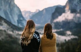Two girls looking across a mountain scene wrapped up warm at Dawn.