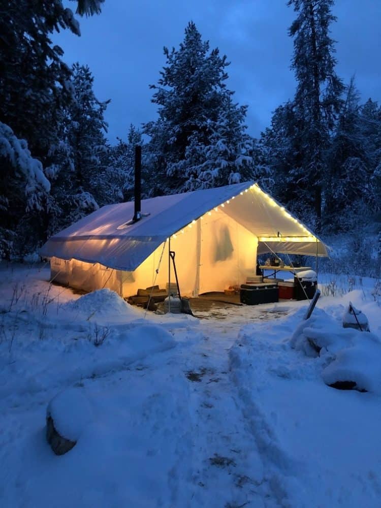 A wall tent set up permanently on a wooden platform in the forest at the beginning of winter.
