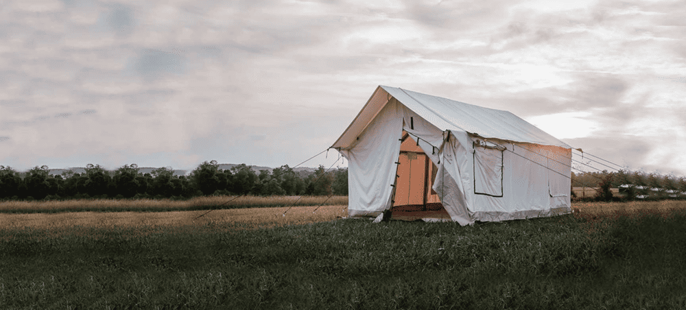 An Empty Wall tent set up in a field at sunset.