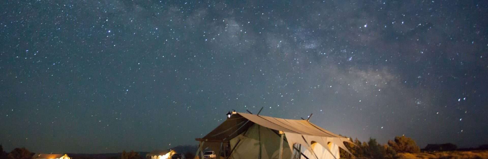 Wall tent set up in scrub land under a starry sky at night.