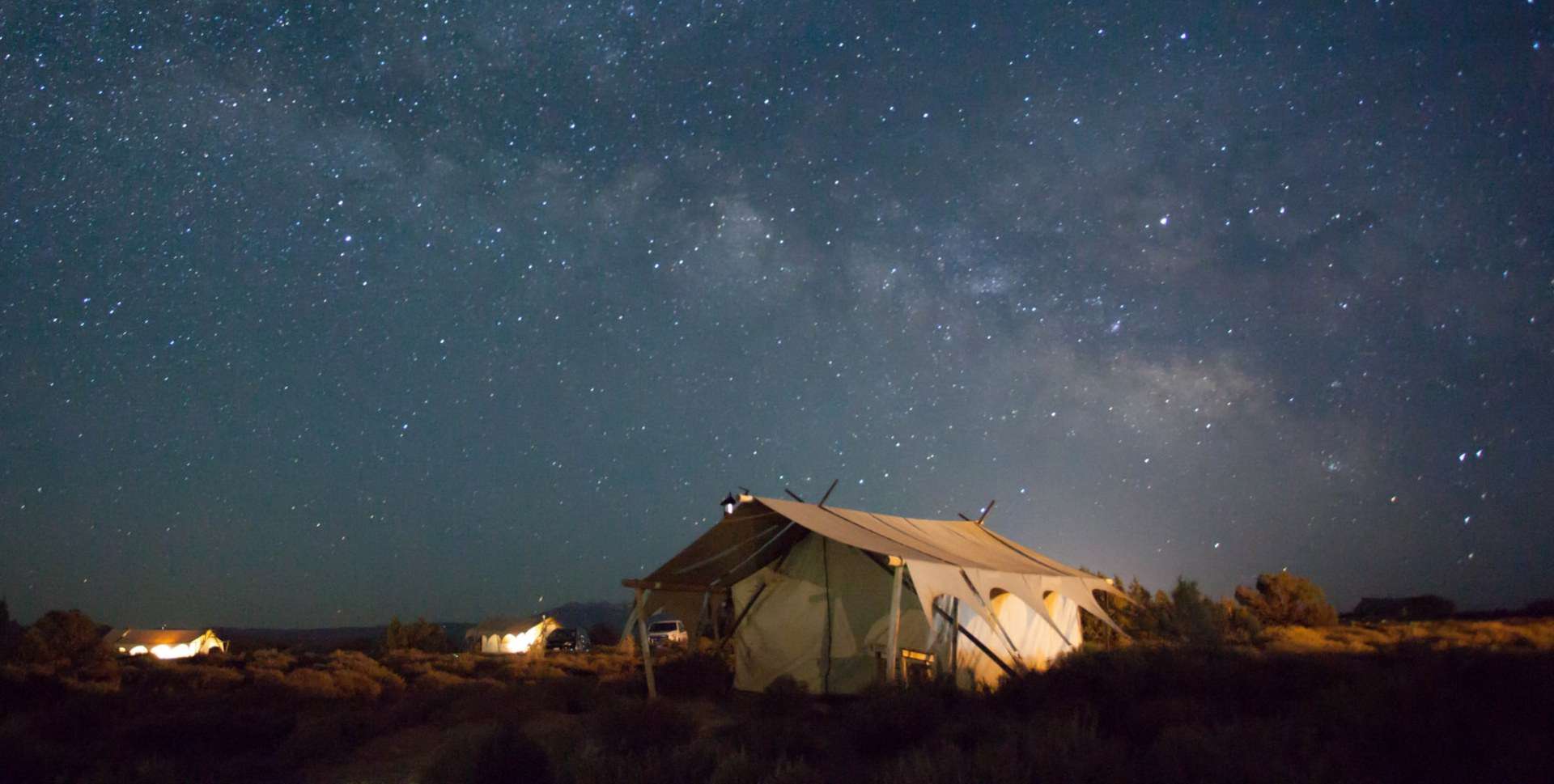 Wall tent set up in scrub land under a starry sky at night.
