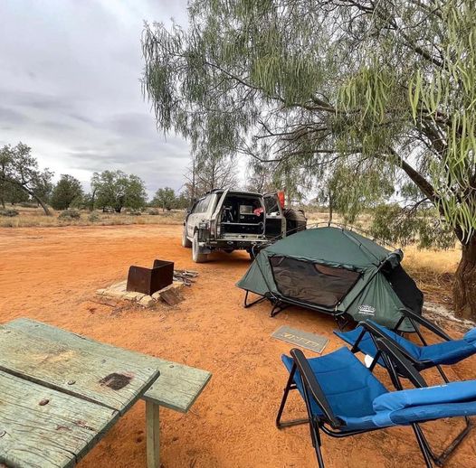 Double camp cot set up in a desert campsite with just a table and chairs beside the ute.