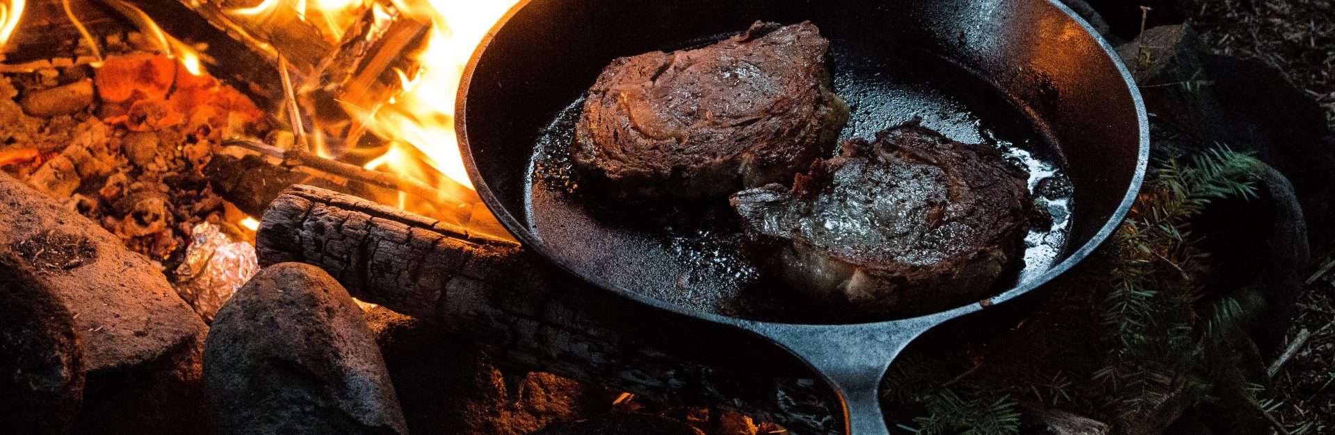 meat cooking in a cast-iron frying pan on a campfire