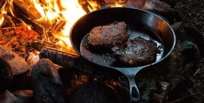 meat cooking in a cast-iron frying pan on a campfire