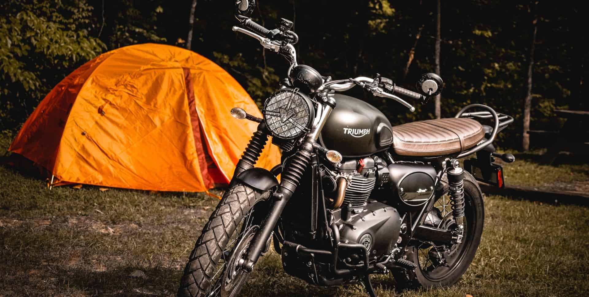 Triumph motorcycle outside an orange motorcycle camping tent in a campsite