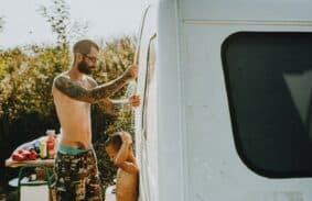 A man showing his child how to shower while camping outdoors