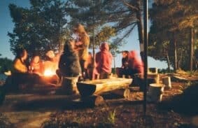 Campers sitting around a portable propane fire pit on a cold night outdoors