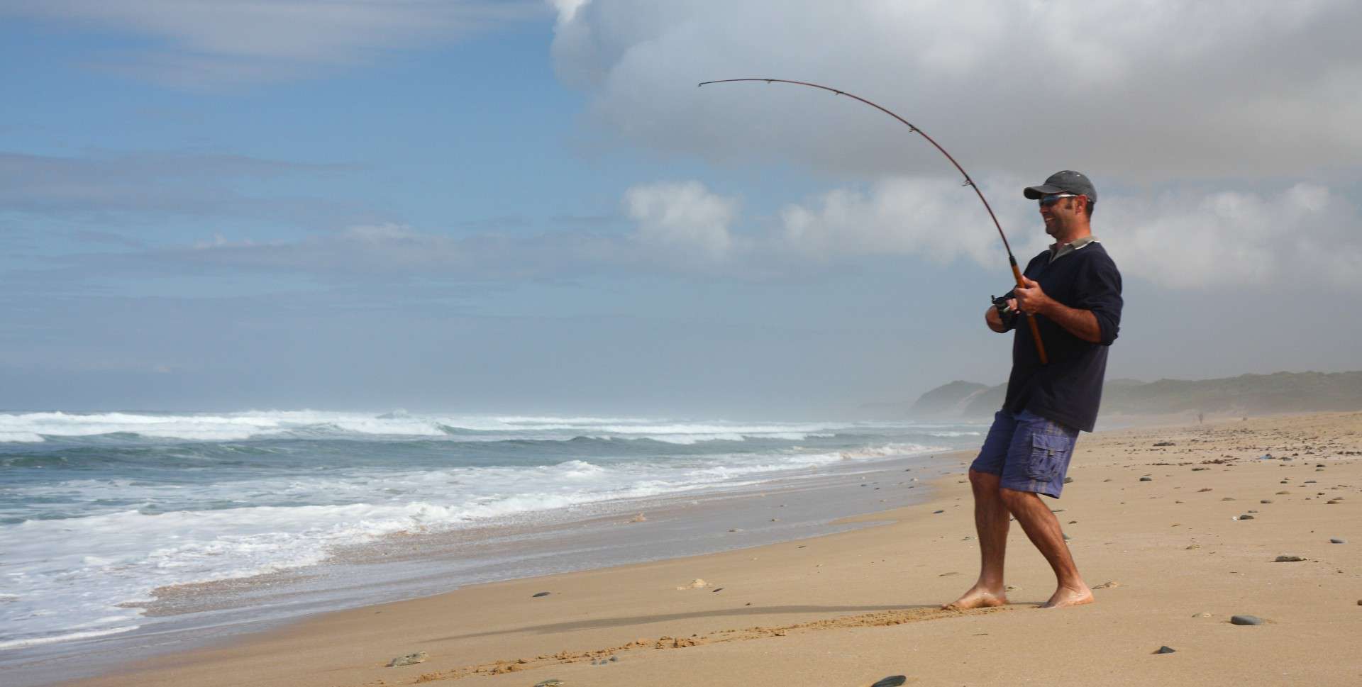 A fisherman surf fishing at a beach using a great fishing rod